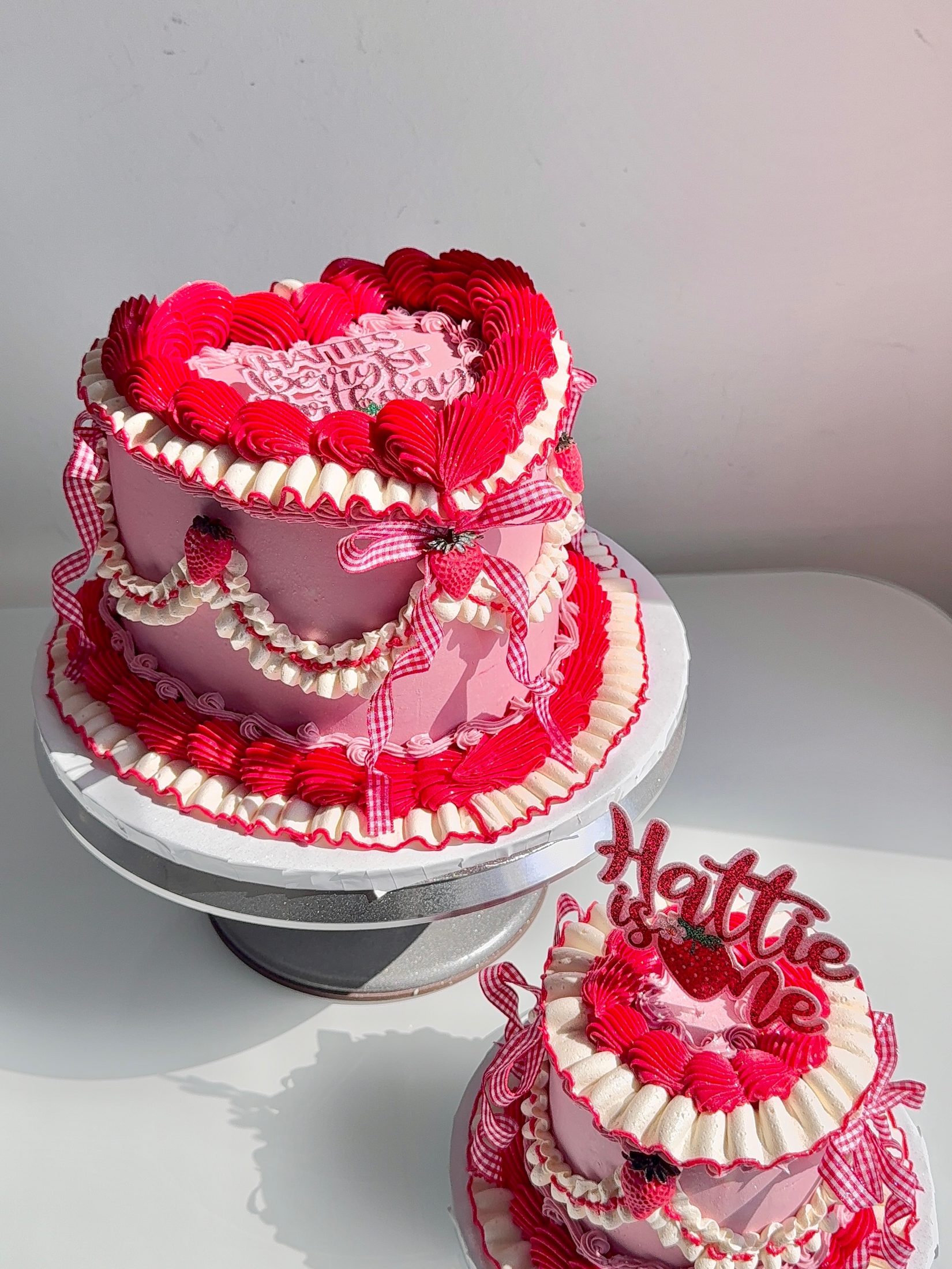Two heart-shaped celebration cakes in red and pink buttercream by Cookie Kisses